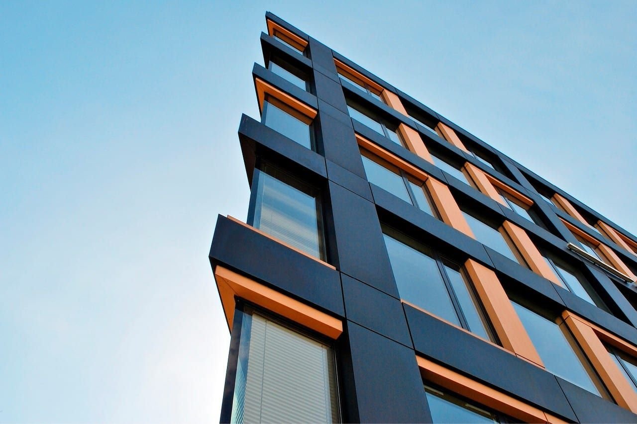 Looking up at a modern commercial building clad in dark facade film with copper-toned window reveals against a clear sky.