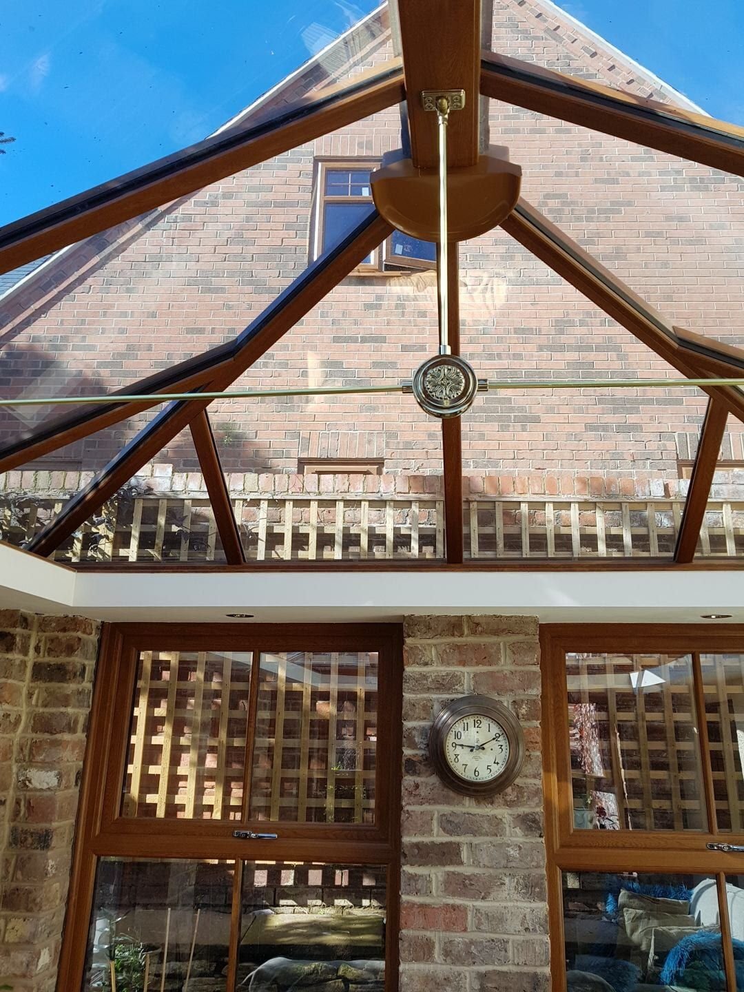 Glass conservatory roof lantern with film applied, oak-framed glazing bars, brick house visible through the glass.