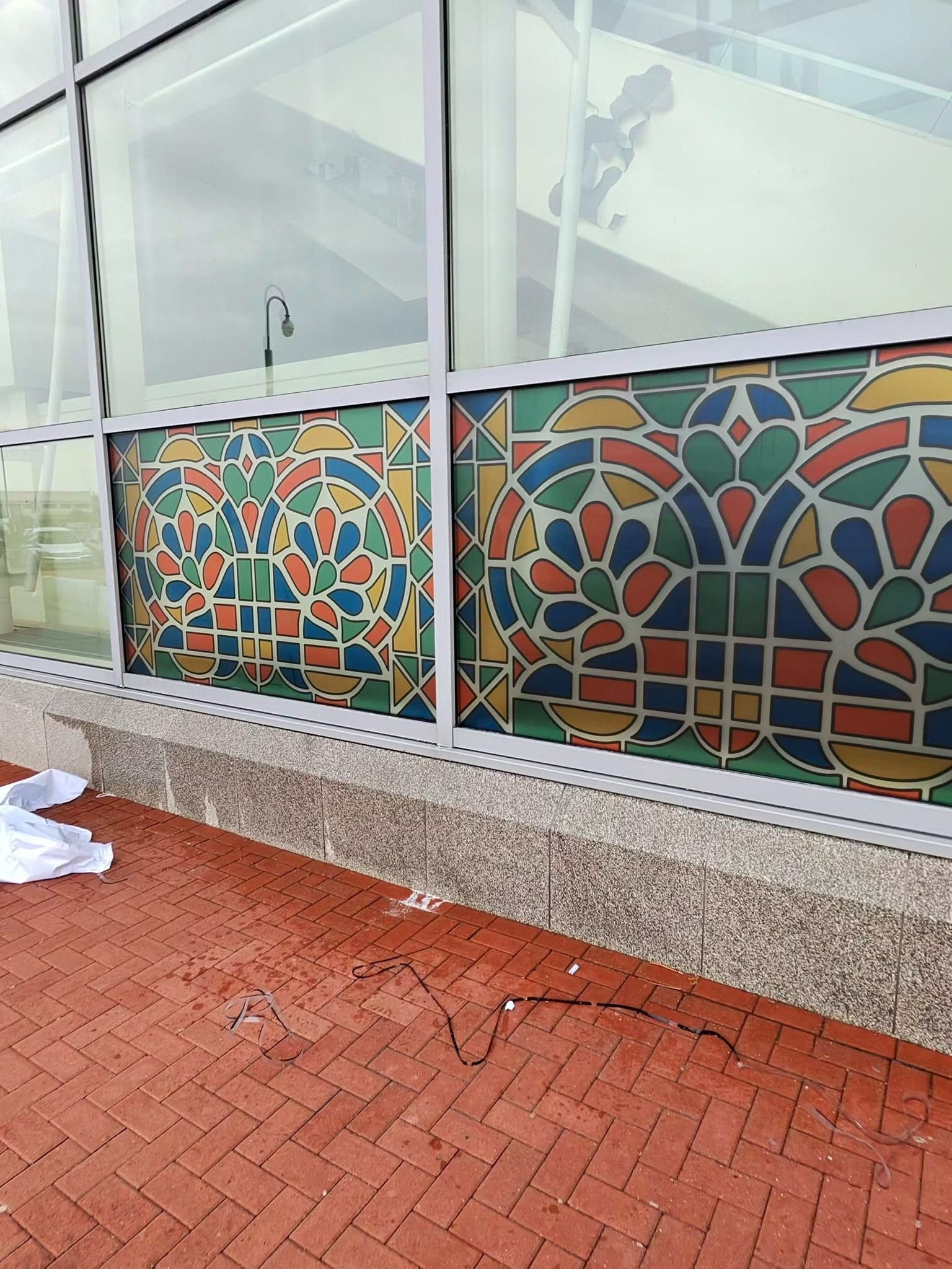 Commercial glazing with a colourful geometric stained-glass-style decorative film pattern across the lower window panels.