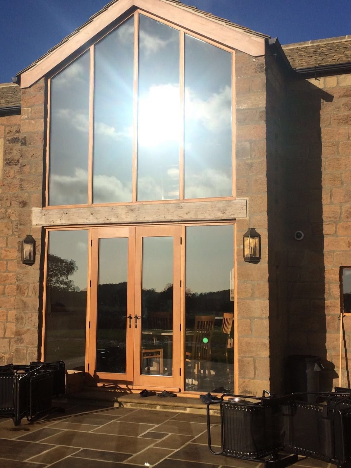 Stone barn conversion with a two-storey gable window and French doors finished in reflective solar film, sunlit exterior.