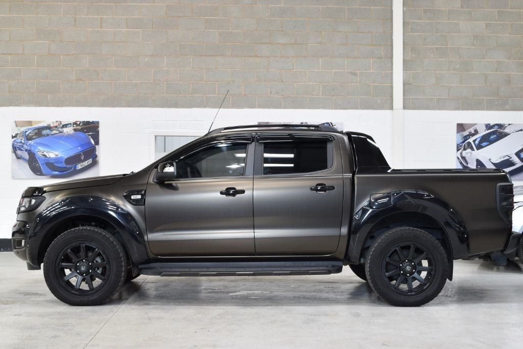 Dark grey matte-wrapped Ford Ranger pickup, side profile, in a studio/showroom setting.